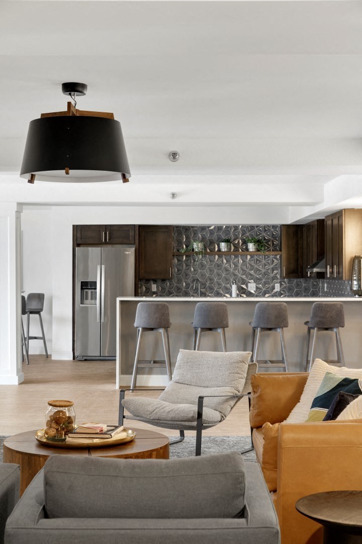 the living room and kitchen of a home with a gray couch and stools