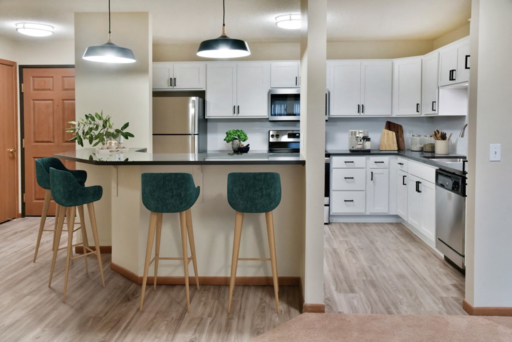 a kitchen with white cabinets and a bar with three stools