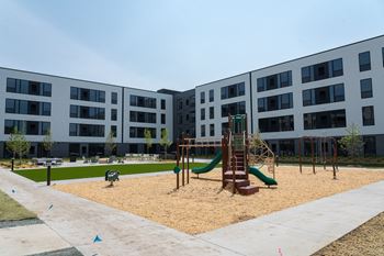 A playground with a green slide and sandbox in front of a building.