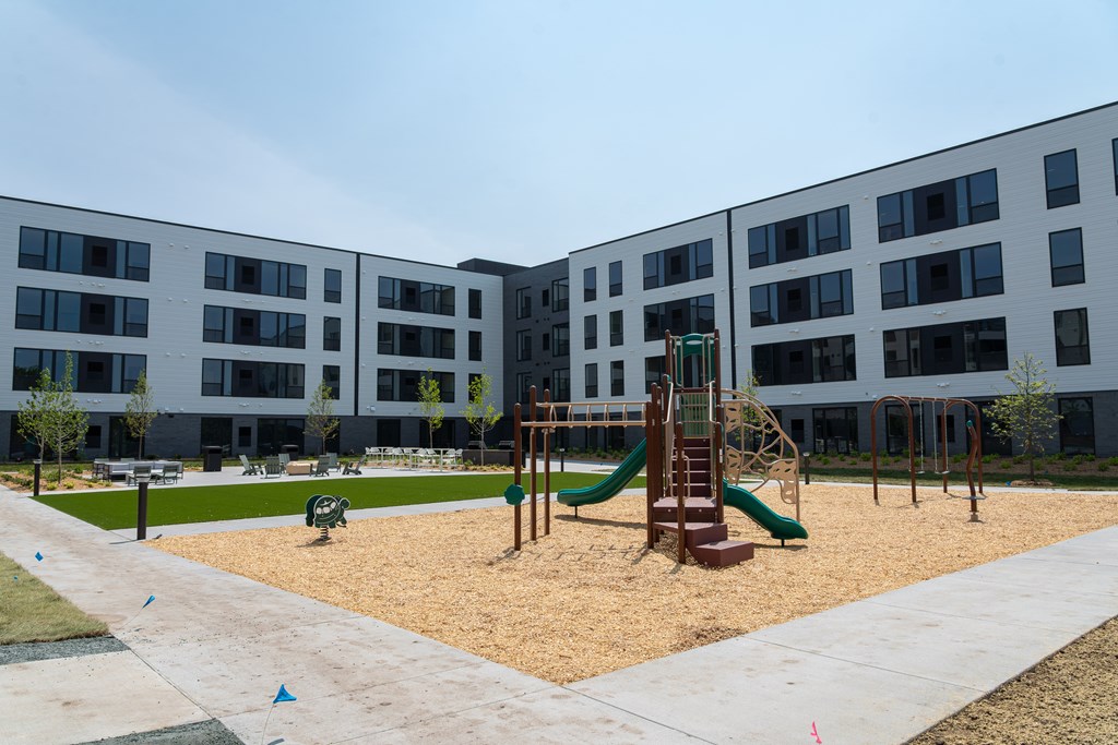 A playground with a green slide and sandbox in front of a building.