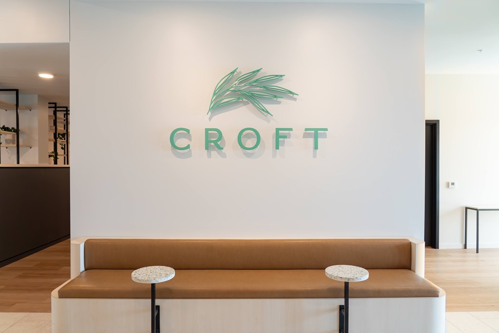 A white wall with a logo and a brown couch in front of it.