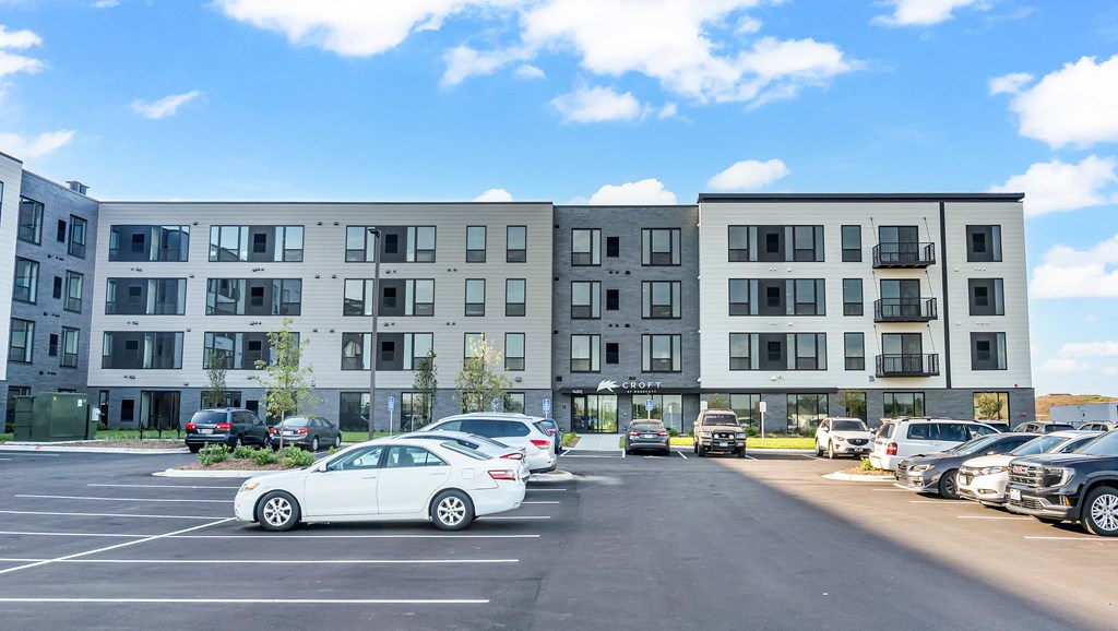 A white car is parked in a parking lot in front of a large apartment building.