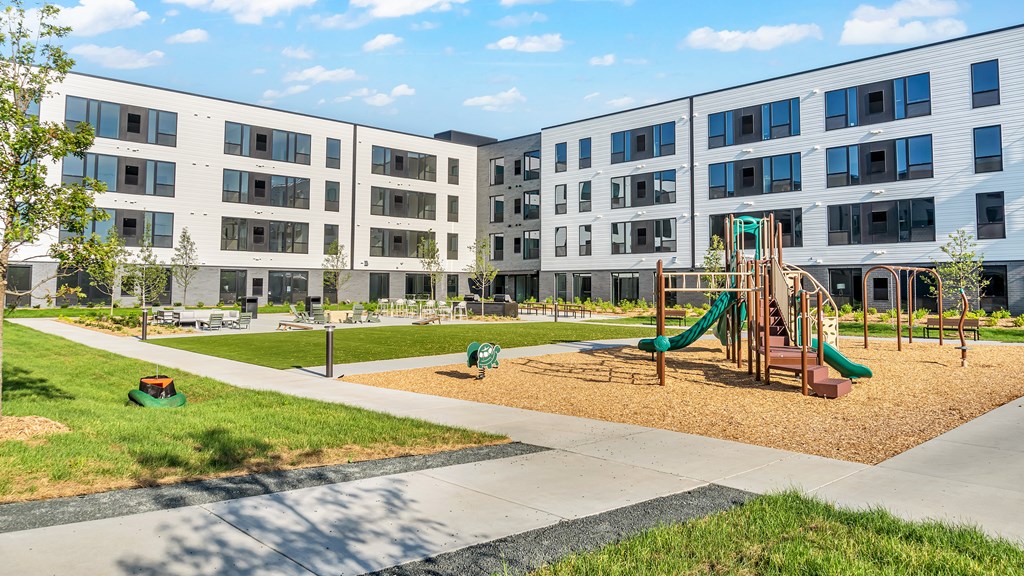 A playground with a slide and a green lawn in front of apartment buildings.