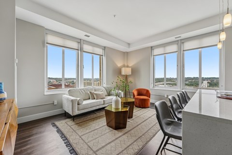 A living room with a white couch, a brown coffee table, and a large window with a view of the city.