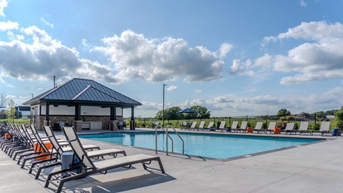 A pool with sun loungers and a pavilion is surrounded by a fence. at The Edison at Maple Grove, Minnesota, 55311