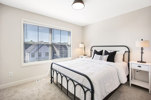 A bedroom with a large bed, nightstand, and window with blinds.