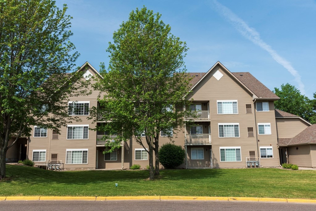 a large apartment building with tan siding and a large tree in front of it
