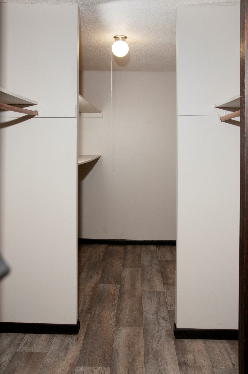 a walk in closet with white walls and wood floors