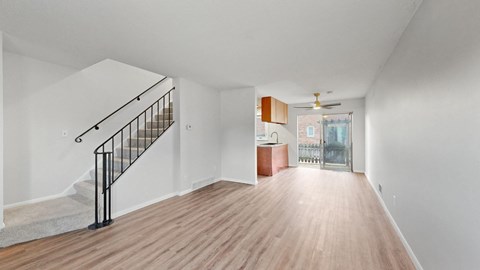 A spacious room with a wooden floor and a staircase with a black railing.
