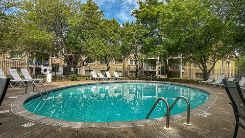 A round swimming pool surrounded by trees and chairs.