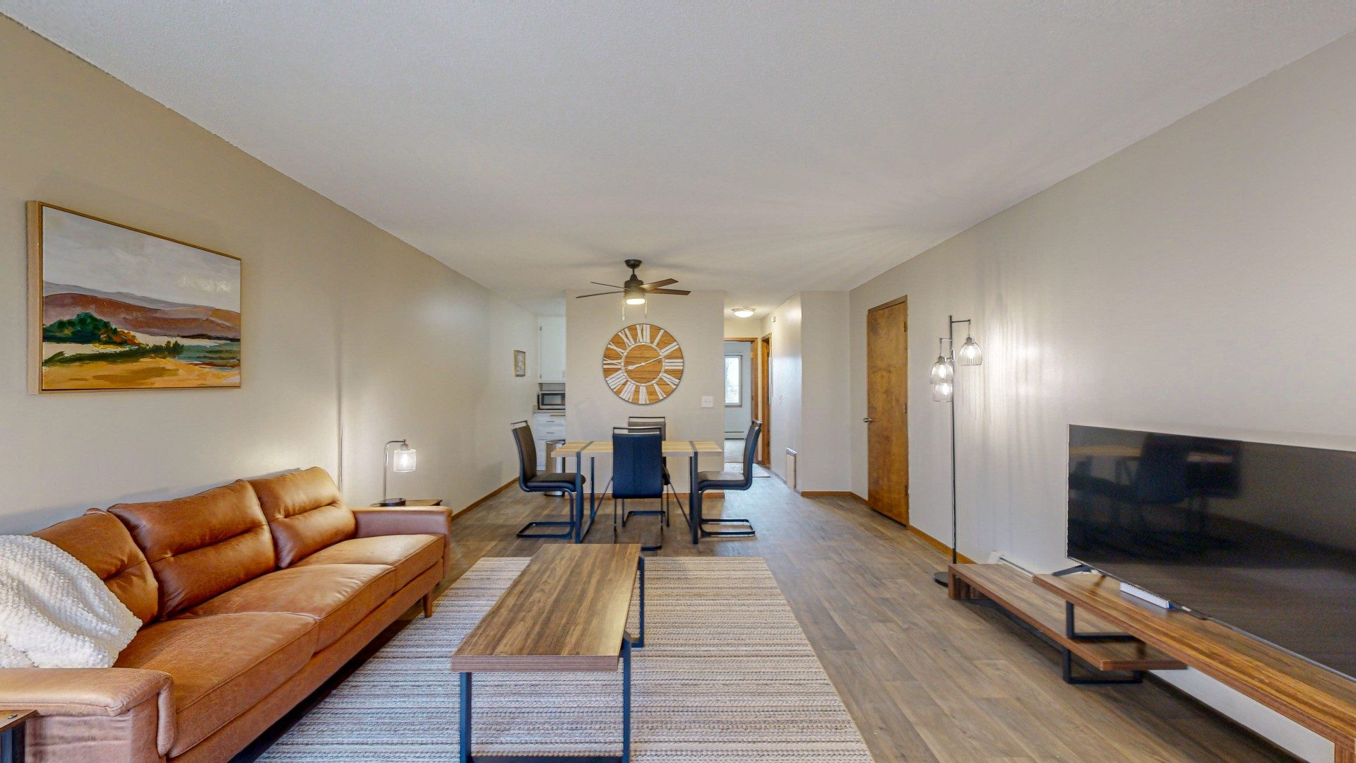 A living room with a brown leather couch and a painting of a landscape on the wall.