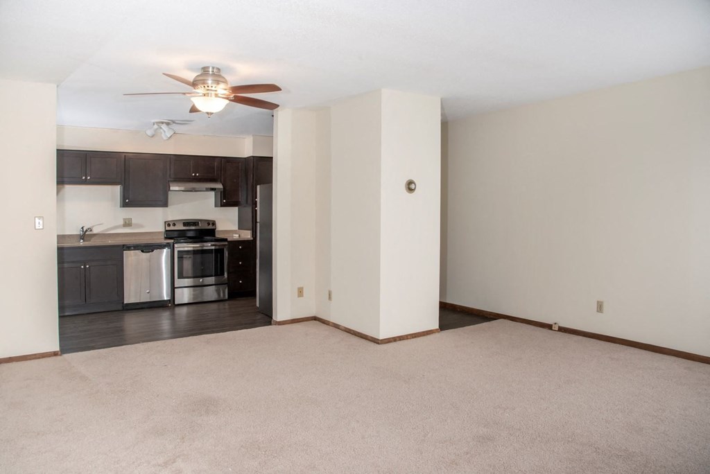an empty living room with a ceiling fan and a kitchen