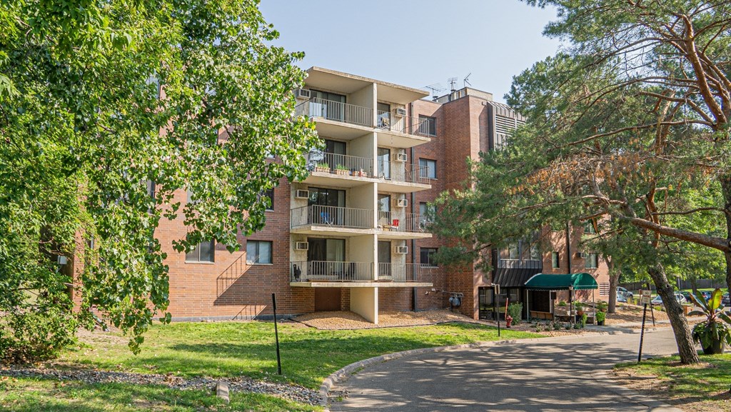 a large brick apartment building with trees and a pathway