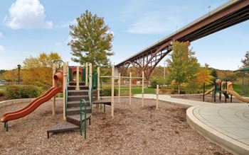 A playground with a slide, swings, and a bridge in the background.