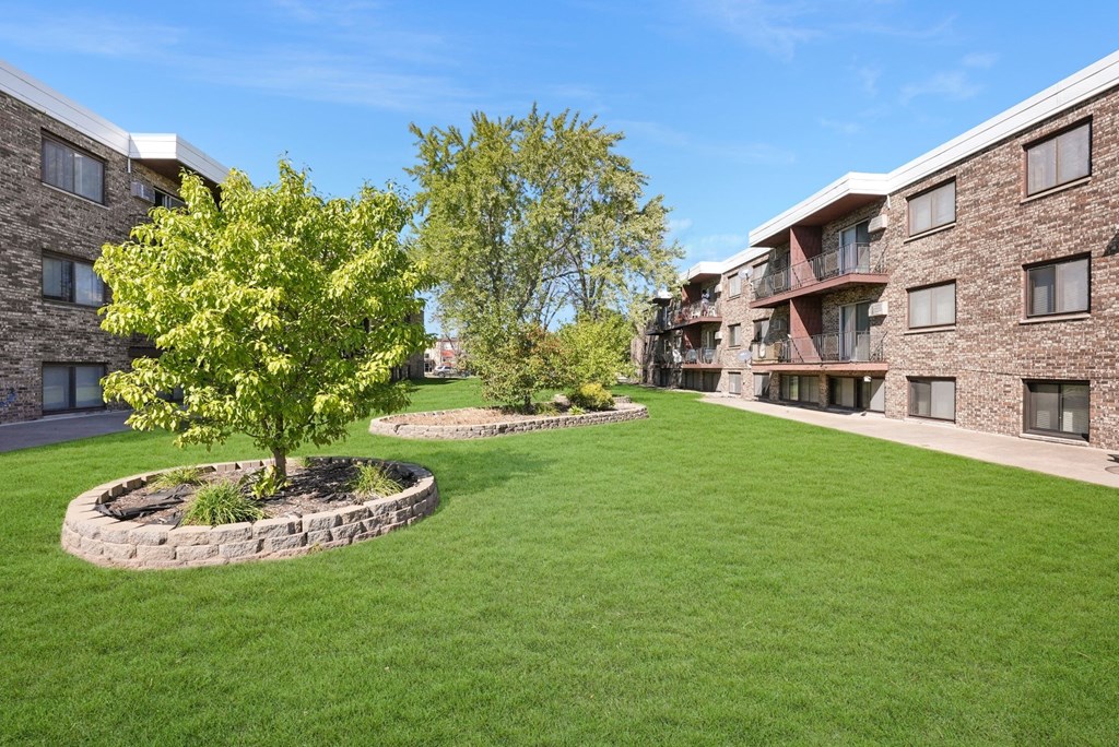 a green lawn in front of a building with trees