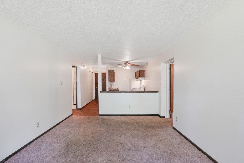an empty living room with a kitchen and a ceiling fan