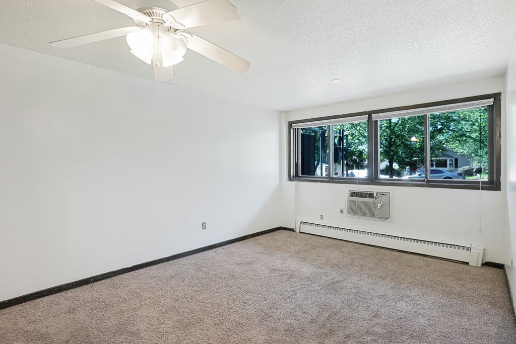 an empty living room with a large window and a ceiling fan