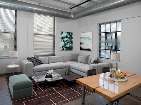 A modern living room with a grey sofa, a green ottoman, a wooden coffee table, and a painting on the wall.