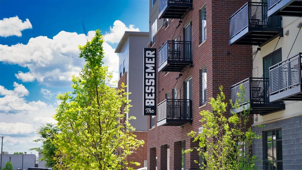 A red brick building with a balcony and a tree in front of it at The Bessemer at Seward Commons Apartments, Minneapolis