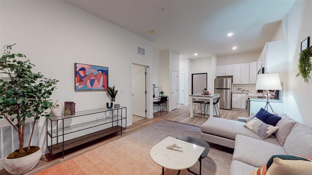 A living room with a grey couch, a coffee table, and a painting on the wall at The Bessemer at Seward Commons Apartments, MN, 55404