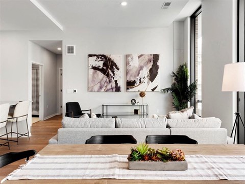 A modern living room with a grey sofa, a wooden table, and a large abstract painting on the wall.