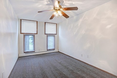 an empty living room with a ceiling fan and two windows