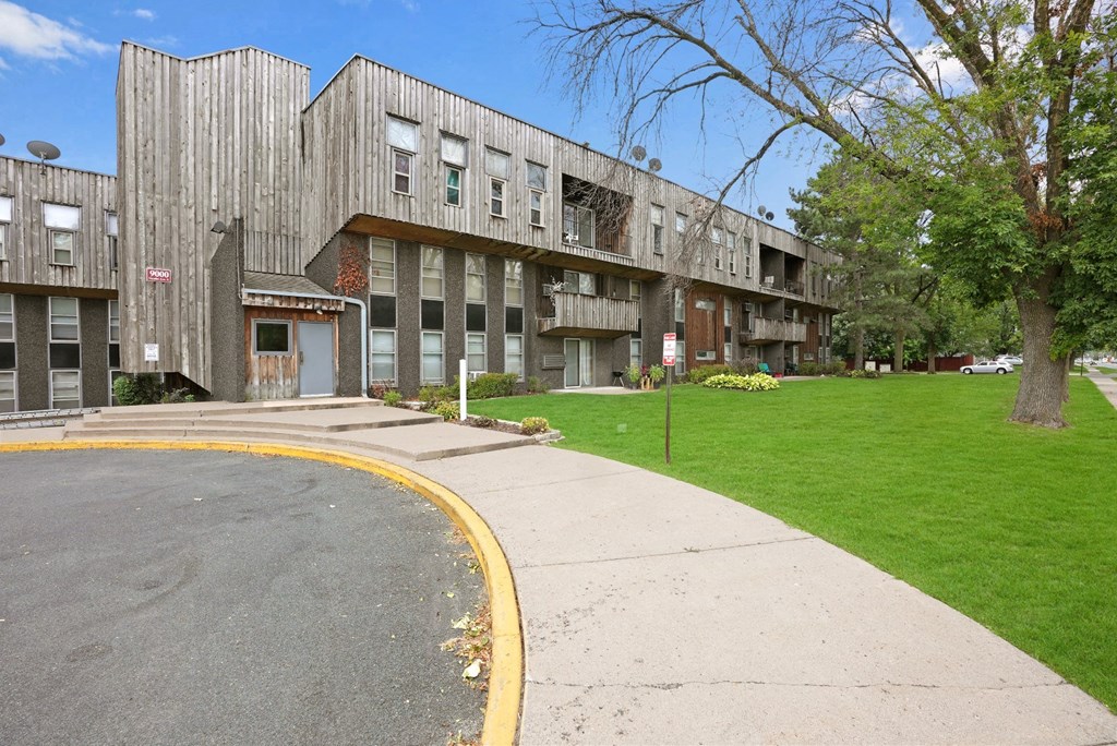 the front of an apartment building with a sidewalk and grass