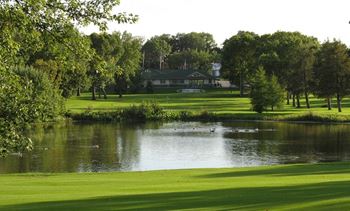 a golf course with a pond in the foreground and a large building in the background