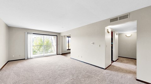 A spacious room with a carpeted floor and a sliding glass door leading to a balcony.