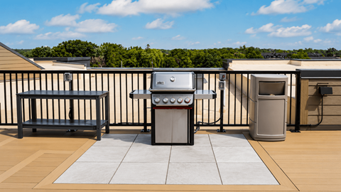 A BBQ grill is on a patio with a bench and a trash can.