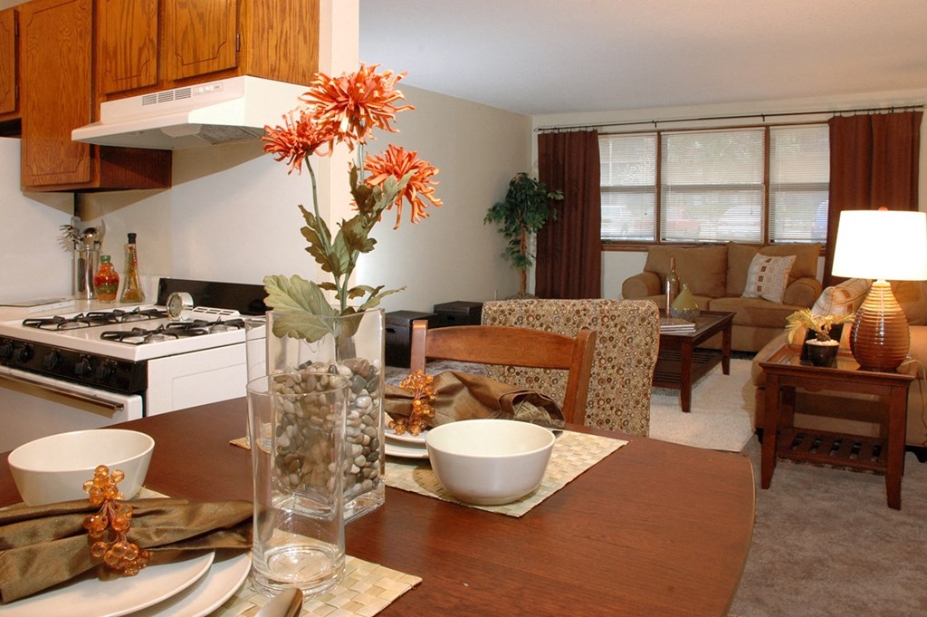 a living room with a wooden table and a kitchen in the background at Point of America Apartments,Brooklyn Park, Minnesota