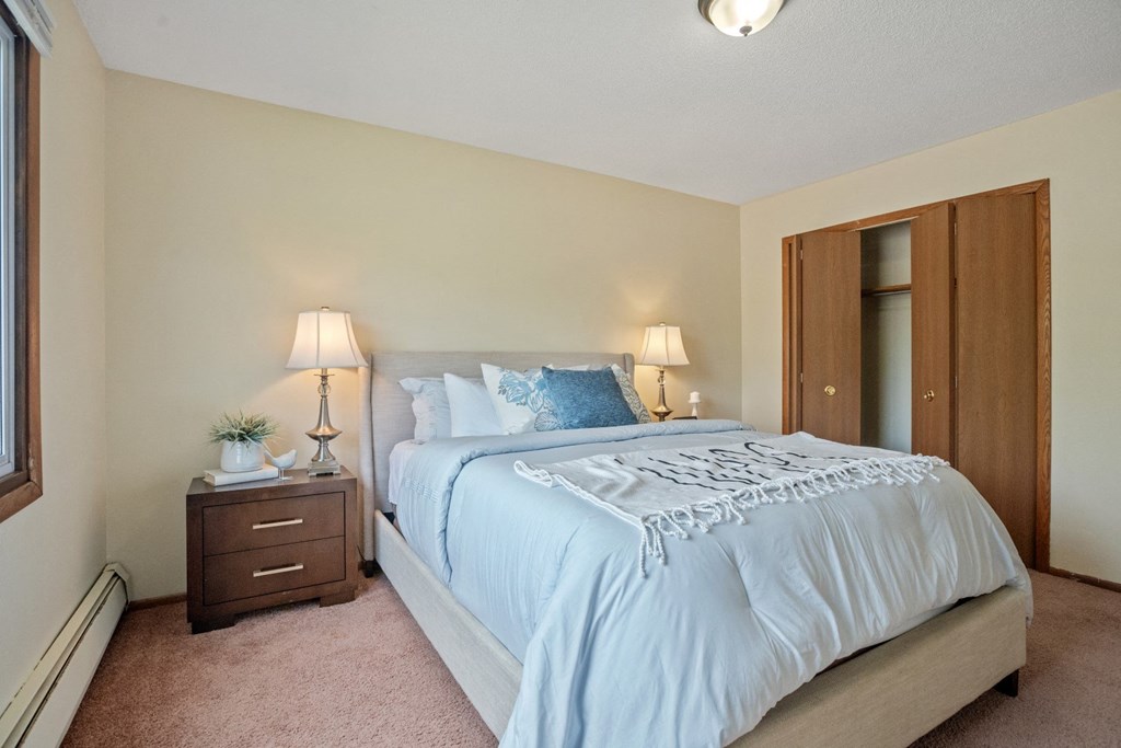 a bedroom with a large bed and a nightstand with two lamps at Point of America Apartments,Brooklyn Park, Minnesota