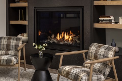 A fireplace with a fire burning inside and two chairs with plaid upholstery in front of it.