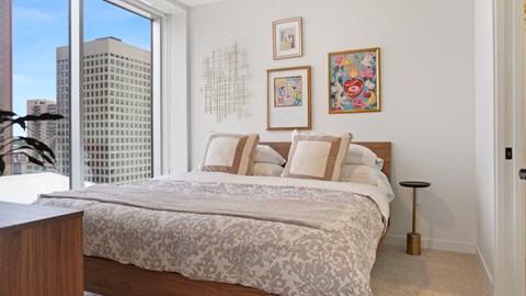 A bedroom with a large bed and a city view through the window.