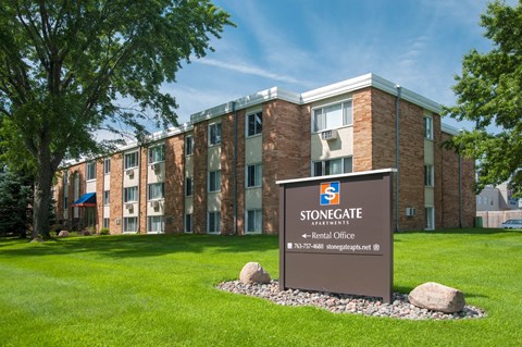 a stonegate apartment building with a sign in the grass