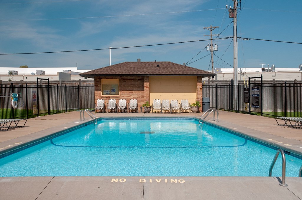 a swimming pool with a small brick pool house with chairs around it
