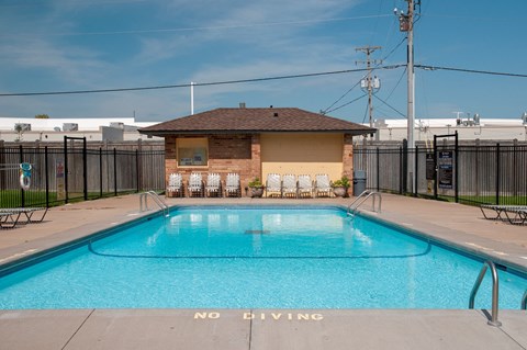 a swimming pool with a small brick pool house with chairs around it
