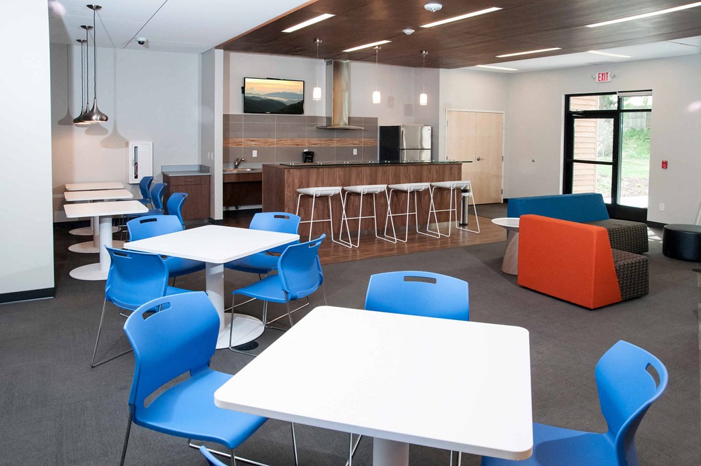 a room with white tables and blue chairs and a kitchen in the background