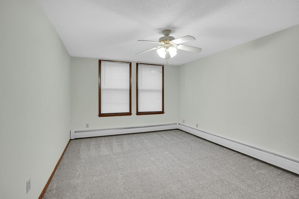 an empty living room with a ceiling fan and two windows