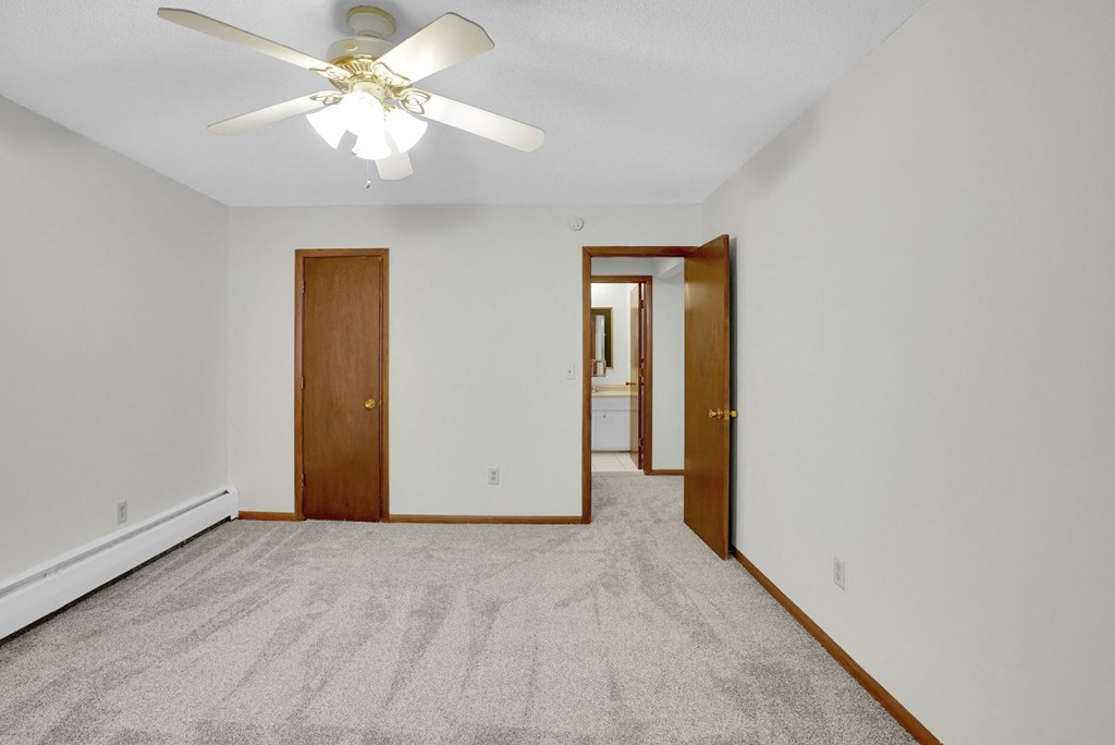 a bedroom with white walls and a ceiling fan and a door to a hallway