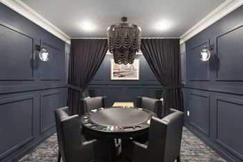 A black poker table is surrounded by black chairs in a room with dark walls at The Barnum Apartments, Minnesota, 55110