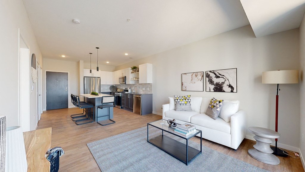a living area with a couch coffee table and a kitchen in the background