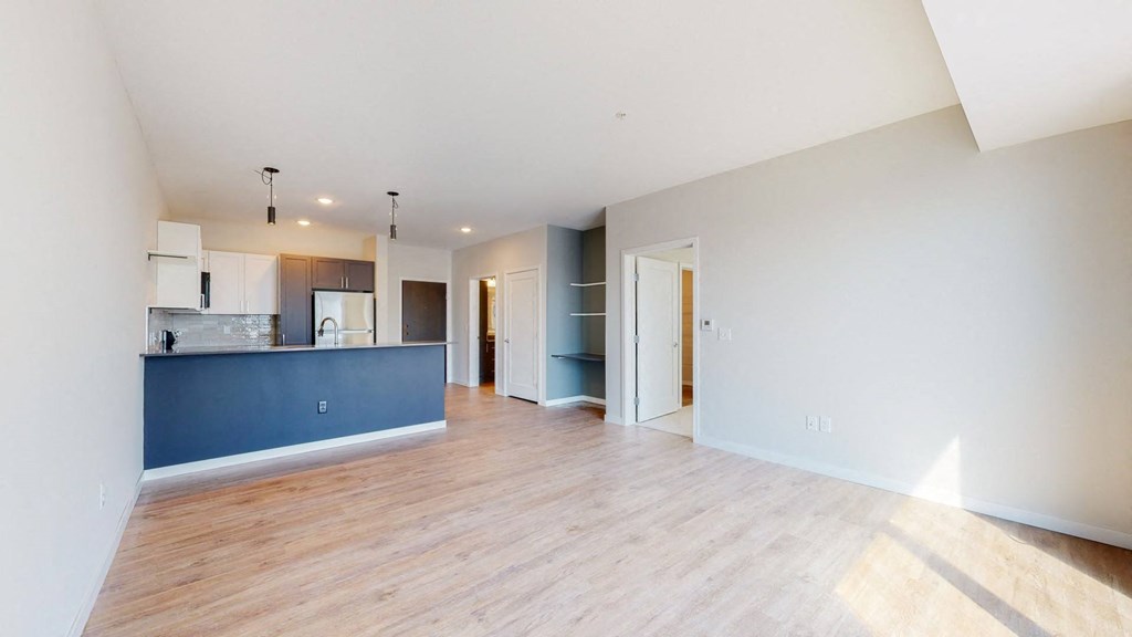 an empty living room with a kitchen in the background