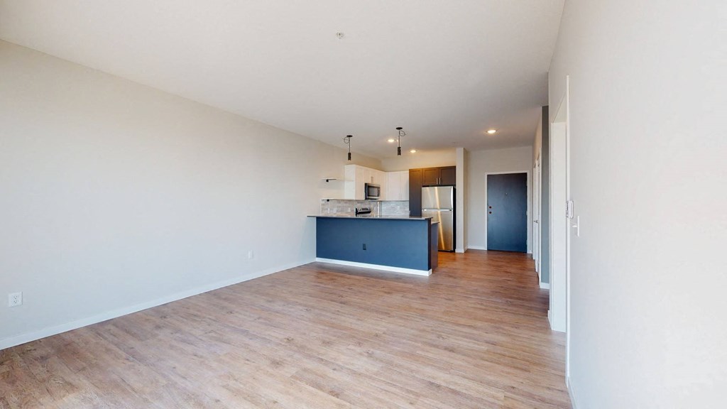 an empty living room with a kitchen in the background