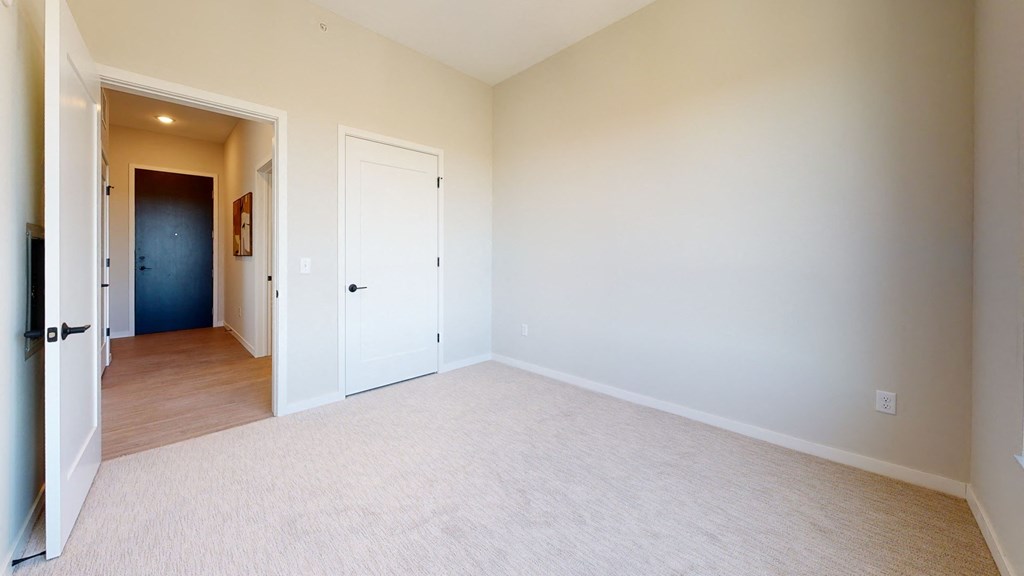 a bedroom with white carpet and a door to a hallway