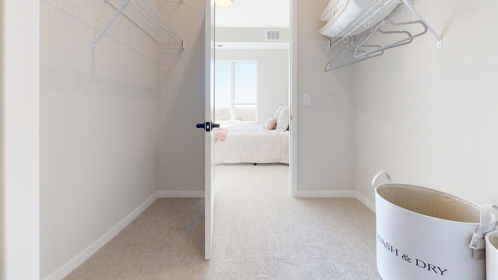 a walk in closet in a bedroom with a bed in the background