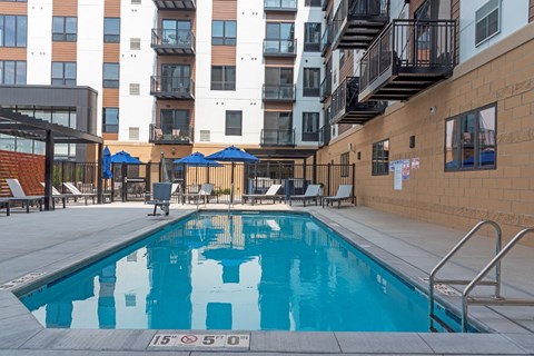 a swimming pool with chairs and umbrellas in front of an apartment building