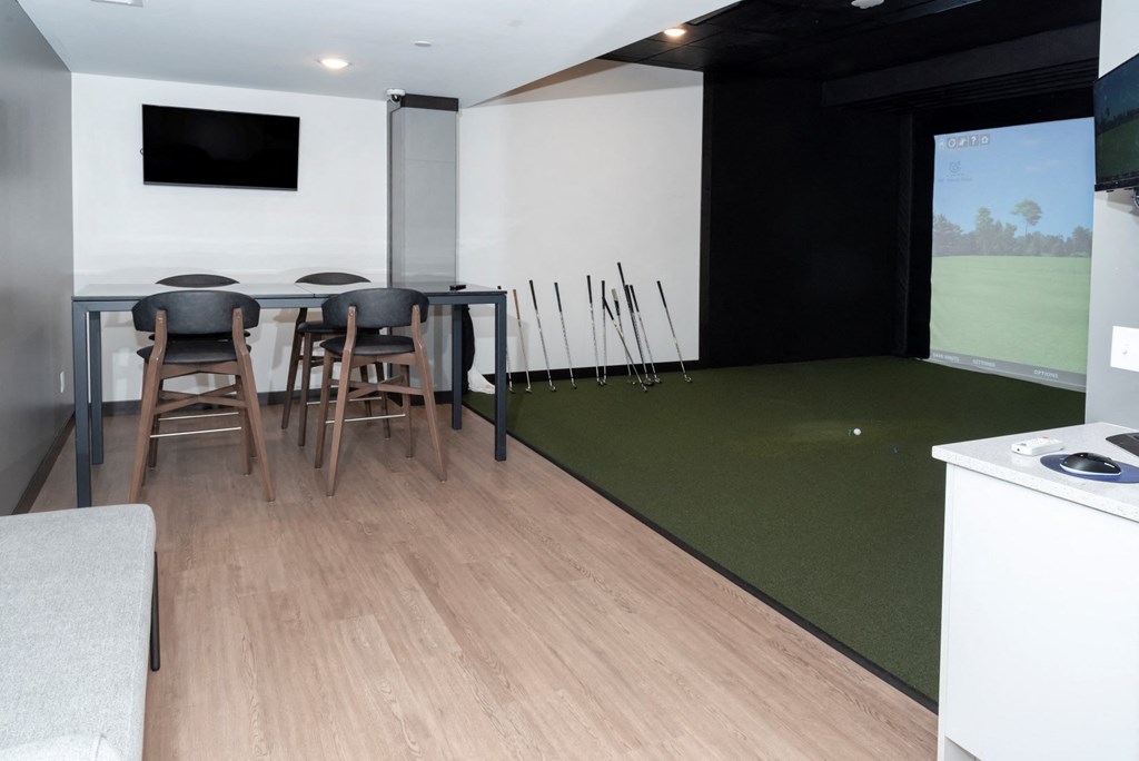 a room with a table and chairs and a golf simulator in the corner