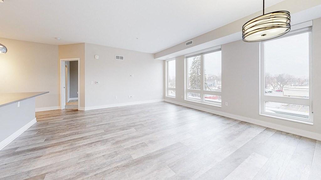 the living room with large windows and a kitchen to the right