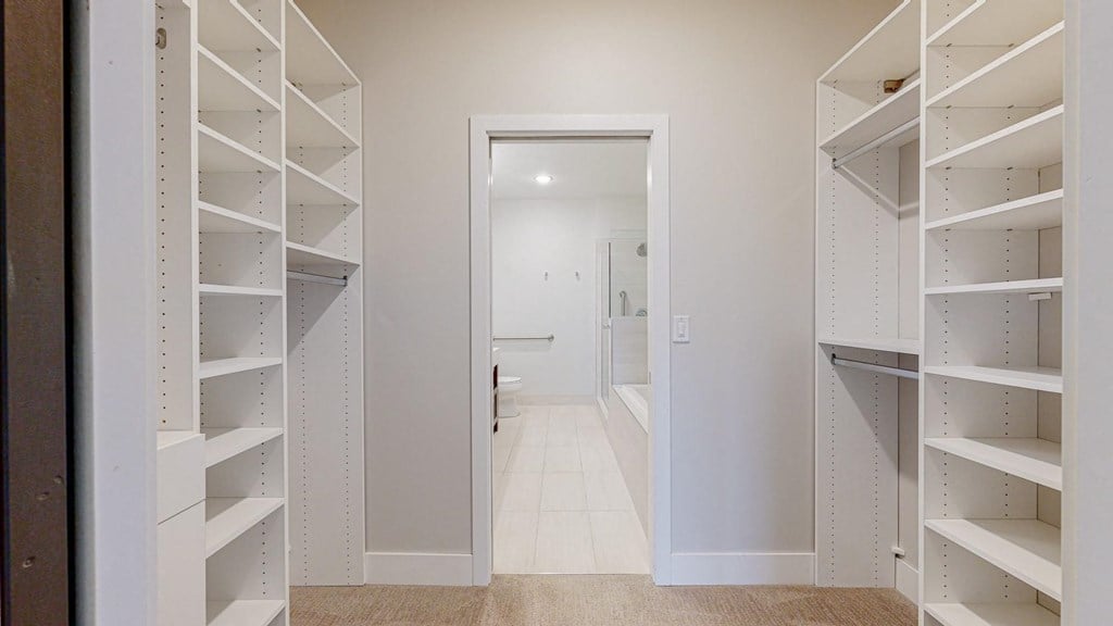 a spacious walk in closet with white shelving and a white bathtub